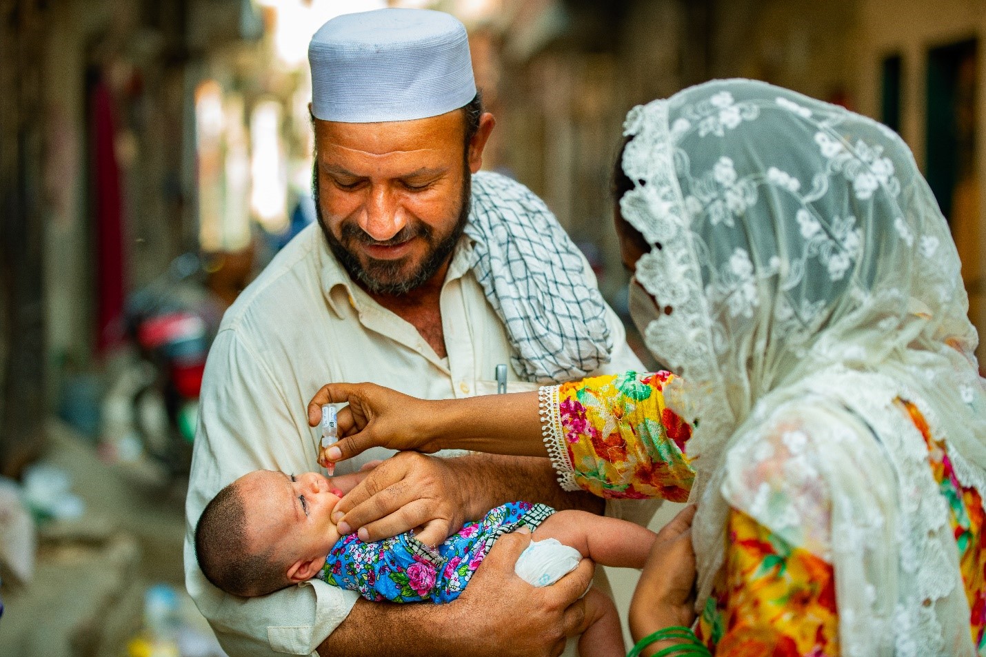 Polio staff Husna Bibi (24) is vaccinating a four-month old girl on the lap of his father in UC-117, Maraghzar Colony, Lahore, Pakistan during case response in August. Photo: 2020/UNICEF Pakistan/Mehdi Bukhari