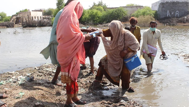  Lady Health Worker Sita helping Hawa to get out of the muddy water  LHW Hawa vaccinating a child in Sindhri, Mirpur Khash