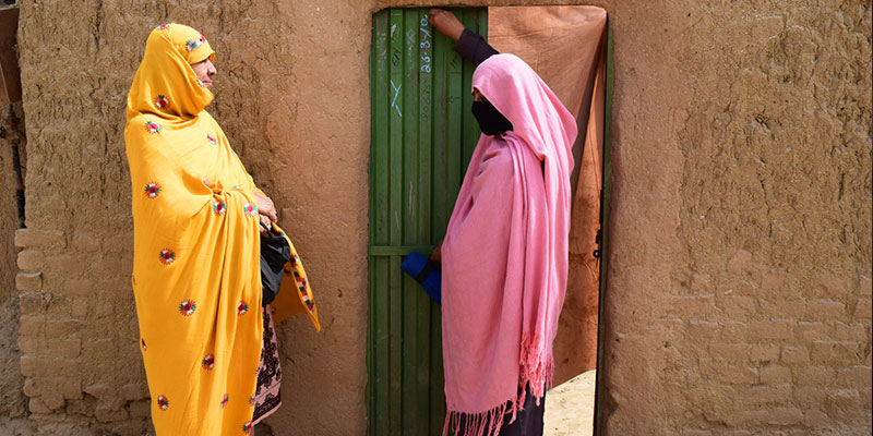 Gulbashra marking the door of a house with her mother-in-law supporting her